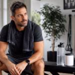 Mann nach dem Training mit Wasser, Widerstandsbändern und einem neutralen Behälter für Nahrungsergänzungsmittel zur Unterstützung der Durchblutung